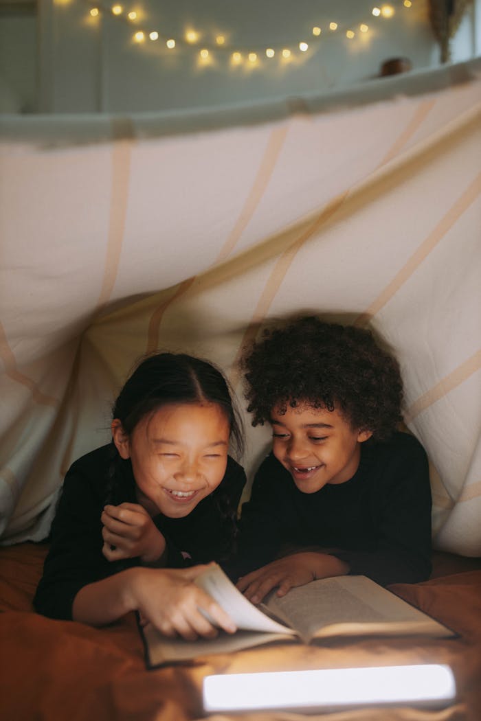 our-story Two children happily reading under a cozy blanket fort with warm lighting.
